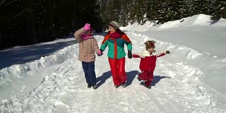 快乐的家庭在冬天的雪山森林里玩耍。妈妈和她的两个孩子。他们高兴地穿过雪地跑向照相机。