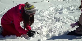 快乐的家庭在冬天的雪山森林里玩耍。妈妈和她的两个孩子扔雪球。做一个雪人。他们笑了。
