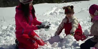 快乐的家庭在冬天的雪山森林里玩耍。妈妈和她的两个孩子扔雪球。做一个雪人。他们笑了。