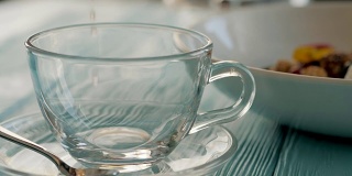 近距离的女服务员在透明的玻璃杯中倒入热腾腾的花草茶。以格兰诺拉麦片为背景的餐厅健康早餐