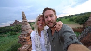 一对夫妇在缅甸一座古老的佛教寺庙上自拍。一对夫妇在缅甸蒲甘探索寺庙，在日出时自拍。一对游客夫妇在亚洲自拍视频素材模板下载