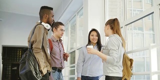 四个多民族的学生站在大学宽敞的白色大厅里积极地交谈。他们正面地笑着，大笑着