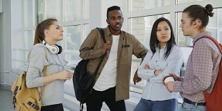 年轻美丽的白人女学生是站在她的三个多民族小组讨论一起在窗户附近积极的方式