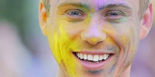 年轻男子的脸在彩色粉末微笑近，在胡里节的乐趣