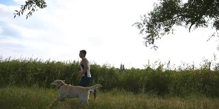 一个年轻人带着他的狗在户外跑步。拉布拉多或金毛猎犬与他的男性主人在大自然中慢跑。健康积极的生活方式。慢动作侧视图特写