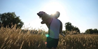 年轻人在田野里用手抚摸他的狗。雄性主人手挽着拉布拉多或金毛寻回犬在草地上散步。与家畜的爱情和友谊。特写慢镜头后视图