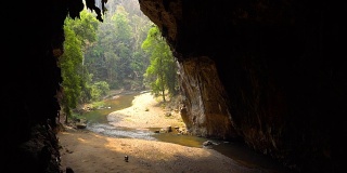 一个老妇人在一个大洞的底部收集蝙蝠粪，洞里有一条河。泰国Tham Lod Cave, Pai。