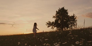 无忧无虑的女孩奔跑在田园诗般的日落夏令草地上，朝着树，实时。春天。
