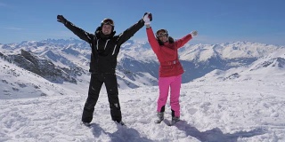 快乐的滑雪情侣站在山顶，举起手