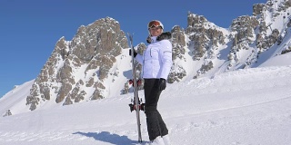 女子滑雪者手持滑雪板站在山的一侧