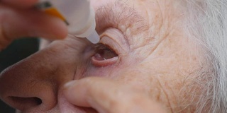 老妇人正在往眼睛里滴药。祖母的画像。医疗保健和医疗理念。特写慢动作