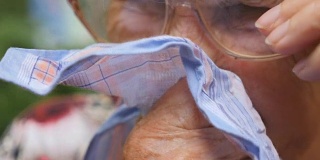 戴眼镜的祖母在户外用手帕擤鼻子。一个生病的老妇人的肖像。特写慢动作