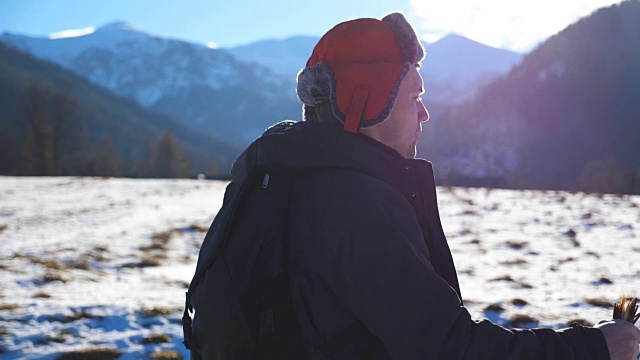 侧面的观点，年轻的徒步旅行者去北欧与棍棒在雪道在野外在山的背景。在阳光明媚的日子里，运动健将在户外运动。健康积极的生活方式。慢镜头