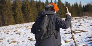 侧面的年轻徒步旅行者与背包和手在雪山上攀登在田野。运动的家伙在阳光明媚的雪地上徒步旅行。健康积极的生活方式。冬季森林的背景。慢镜头