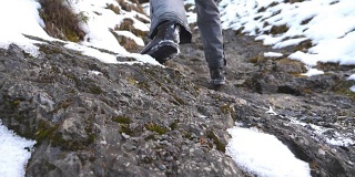 清晨，一个面目全非的人爬上了山道。年轻的男游客走在雪山上。健康积极的生活方式。假日或假期的概念。后视图慢动作