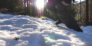 低角度的年轻人慢跑的雪坡在山上松树林。阳光灿烂的一天，一名男性游客在雪山上奔跑。美丽的阳光在背景。旅行的概念。特写慢动作