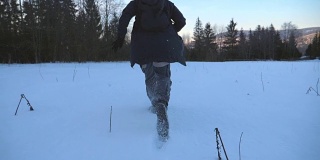 后视图，一个不认识的人慢跑通过雪地草坪在森林的边缘。年轻人晚上在雪地上奔跑，在冬季旅行中享受自由。特写慢动作