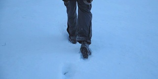 后视图的男性的脚走过在晚上的雪地在田野。一个面目全非的家伙在冬季旅行中享受自由。假期的概念。特写慢动作