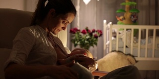 年轻美丽的母亲，在昏暗的灯光下给她的新生儿喂奶。妈妈母乳喂养婴儿。