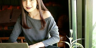 微笑的亚洲妇女使用笔记本电脑在咖啡店
