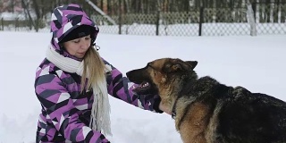 一个穿着冬季夹克的年轻女子在雪地里和一只德国牧羊犬玩耍。