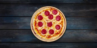 旋转的意大利辣香肠披萨在一个木制支架上，在一个深色的木制背景。俯视图中心方向