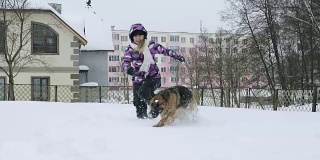一个穿着冬季夹克的女人在雪地里和一只德国牧羊犬玩耍