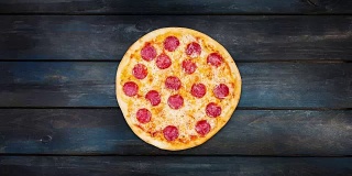 在深色木质背景上旋转经典的意大利辣香肠披萨。俯视图中心方向