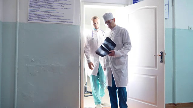 两个白人医生从柜子里出来，看核磁共振成像。男医生通过x光互相展示一些东西。同事们在医院散步。背景。前视图