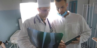 男医生一边使用平板电脑一边互相咨询病人的x光片。医院的医务人员检查x光照片。两位白种人医生观看核磁共振图像并讨论它。前视图