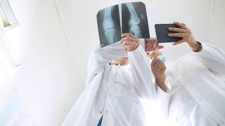 男医生一边使用平板电脑一边互相咨询病人的x光片。医院的医务人员检查x光照片。两位白种人医生观看核磁共振图像并讨论它。低角度视图特写视频素材模板下载