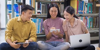 一群年轻的亚洲学生带着书在大学图书馆做研究，学习教育和学校理念