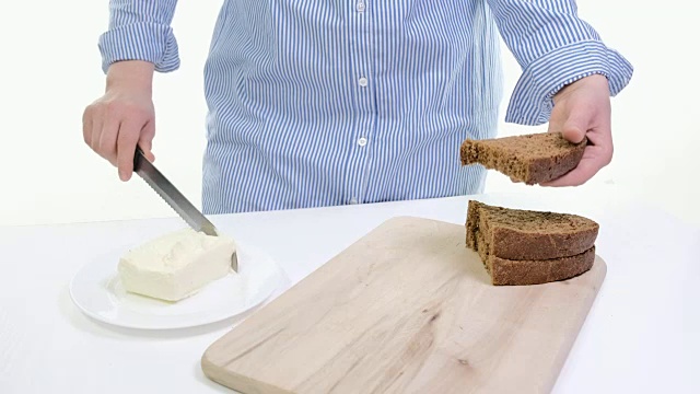 女性的双手在厨房的面包上涂抹黄油的特写。白色backgound