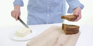 女性的双手在厨房的面包上涂抹黄油的特写。白色backgound