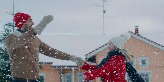 年轻美丽的夫妇在飘落的雪中跳舞和旋转。快乐的男人和女人在他们田园诗般的房子的院子里玩耍。家庭享受冬天。