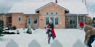 年轻美丽的夫妇互相扔雪球当雪落下。快乐的男人和女人在他们田园诗般的房子的院子里玩雪。家庭享受冬天。