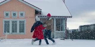 年轻美丽的夫妇在飘落的雪中跳舞和旋转。快乐的男人和女人在他们田园诗般的房子的院子里玩耍。