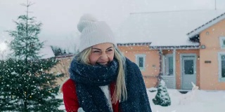 快乐的年轻微笑的女人扔雪球，并被一个击中。穿红外套的女孩和她的伴侣享受冬天。田园小屋后院里的一天。
