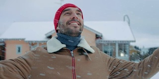 肖像的英俊微笑的男人走在他的后院，举起手臂，在一个美丽的冬日。软雪落。