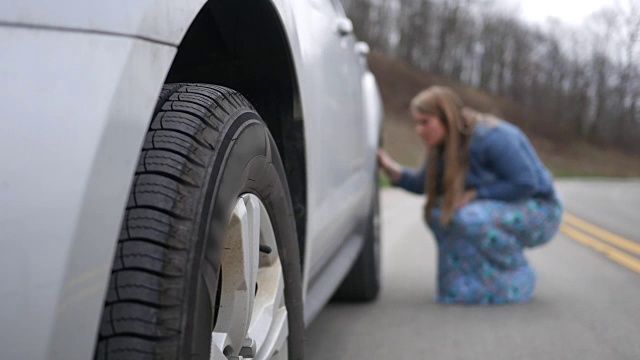 一名妇女在路上检查她的SUV后部瘪了的或损坏的轮胎
