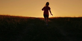 无忧无虑的女孩跑上了山在夕阳的背景。克服困难，首先取得成就