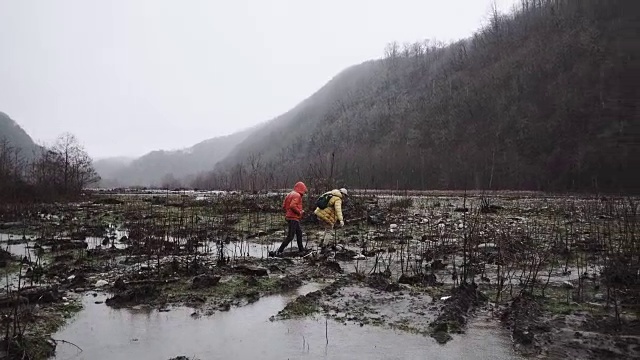 人们和他的朋友们穿着秋天的外套试图在雨中穿过沼泽