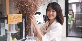 正面:年轻的亚洲咖啡师装饰鲜花和微笑的顾客