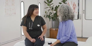 年轻的亚裔护士正在和她的老年病人谈话。