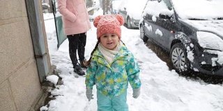 可爱的蹒跚学步的孩子在雪中奔跑，而母亲正在等待