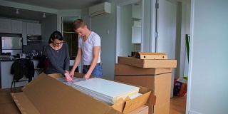 30岁的年轻男子和十几岁的女孩在新公寓里拆箱组装家具