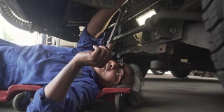 小车从侧面拍摄:亚洲高级汽车技师在车下工作