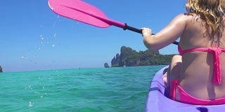 慢动作:在平静的绿松石海水中，一名辨认不出的女性游客划着皮划艇。