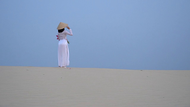 美丽的越南人捧着粉红莲花在白色沙丘沙漠上行走的4K电影，越南