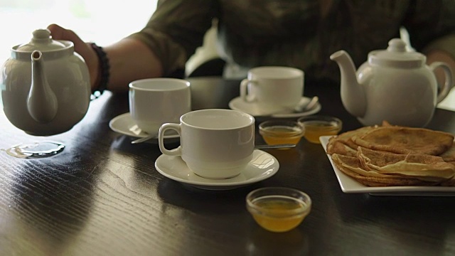 一个男人的手的特写，他正在桌子上吃早餐，倒茶